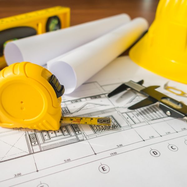 Construction plans with yellow helmet and drawing tools on blueprints